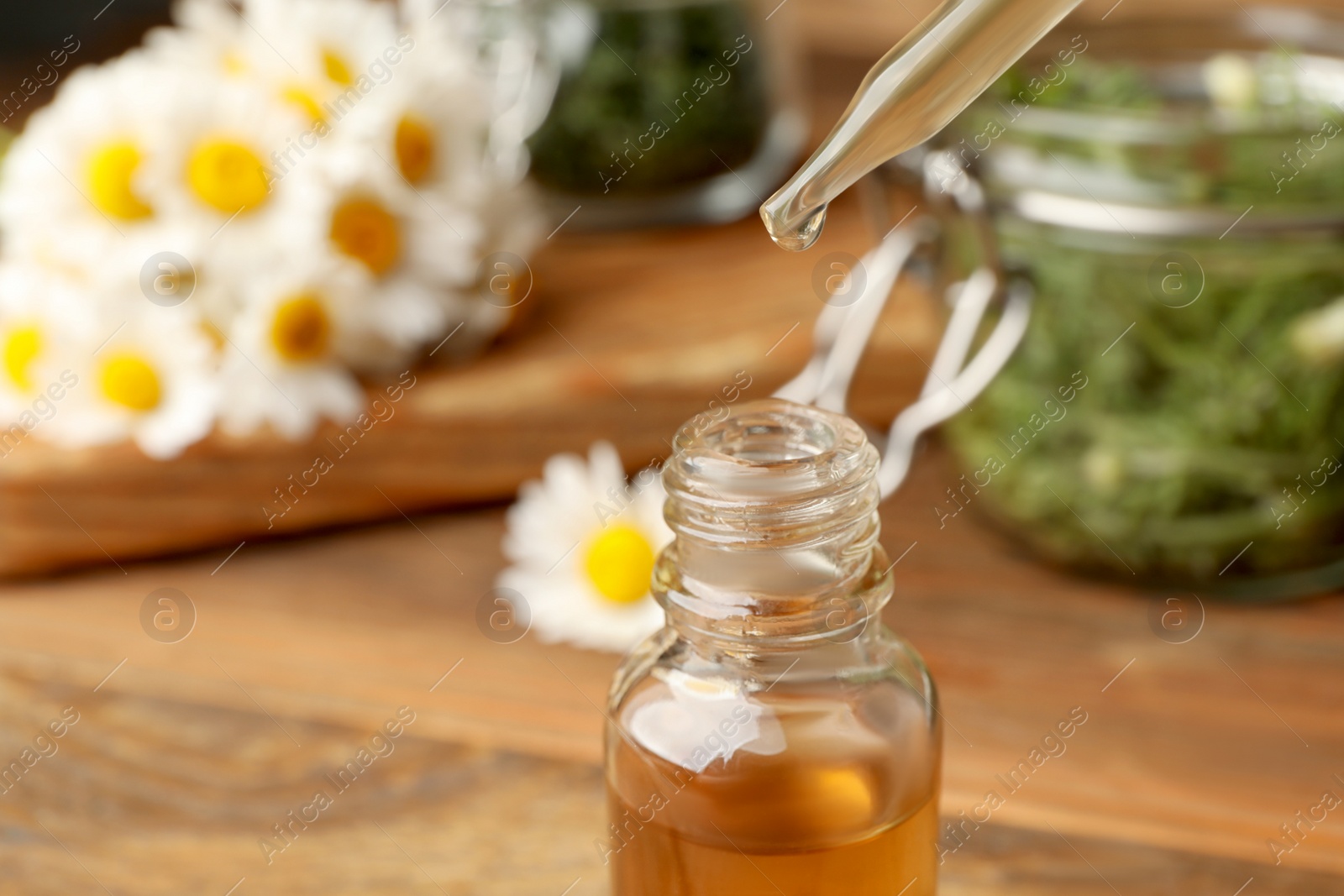 Photo of Pipette with essential oil over bottle on blurred background, closeup. Space for text