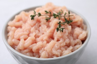 Photo of Fresh raw minced meat and thyme in bowl on light table, closeup
