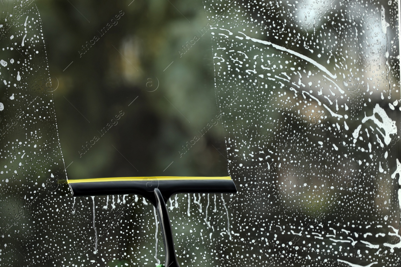 Photo of Cleaning foam from glass with squeegee indoors, closeup