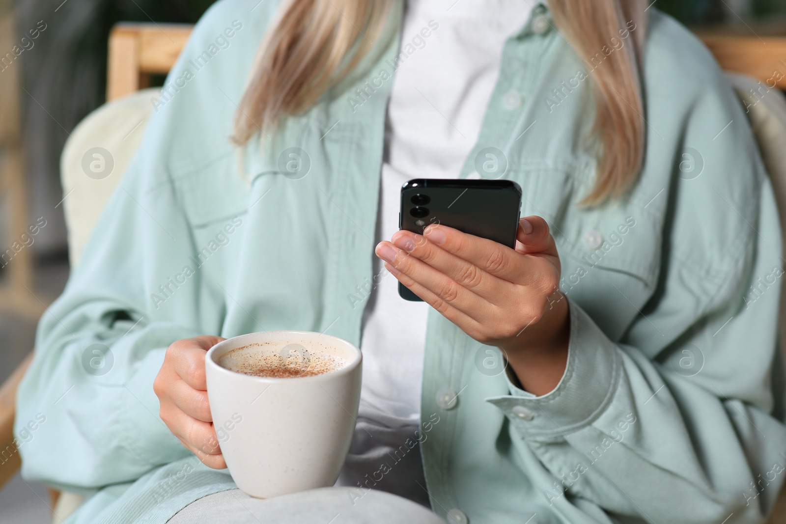 Photo of Woman with smartphone and cup of coffee indoors, closeup