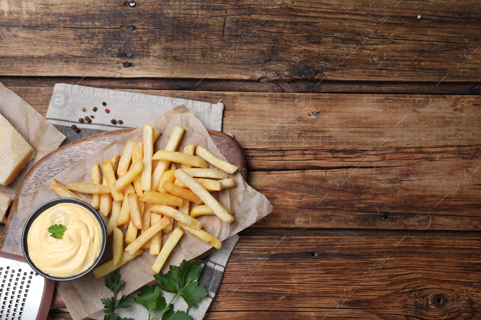 Photo of Delicious French fries and cheese sauce with parsley on wooden table, flat lay. Space for text