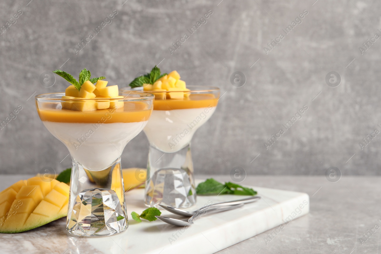 Photo of Delicious panna cotta with mango coulis served on light grey table. Space for text