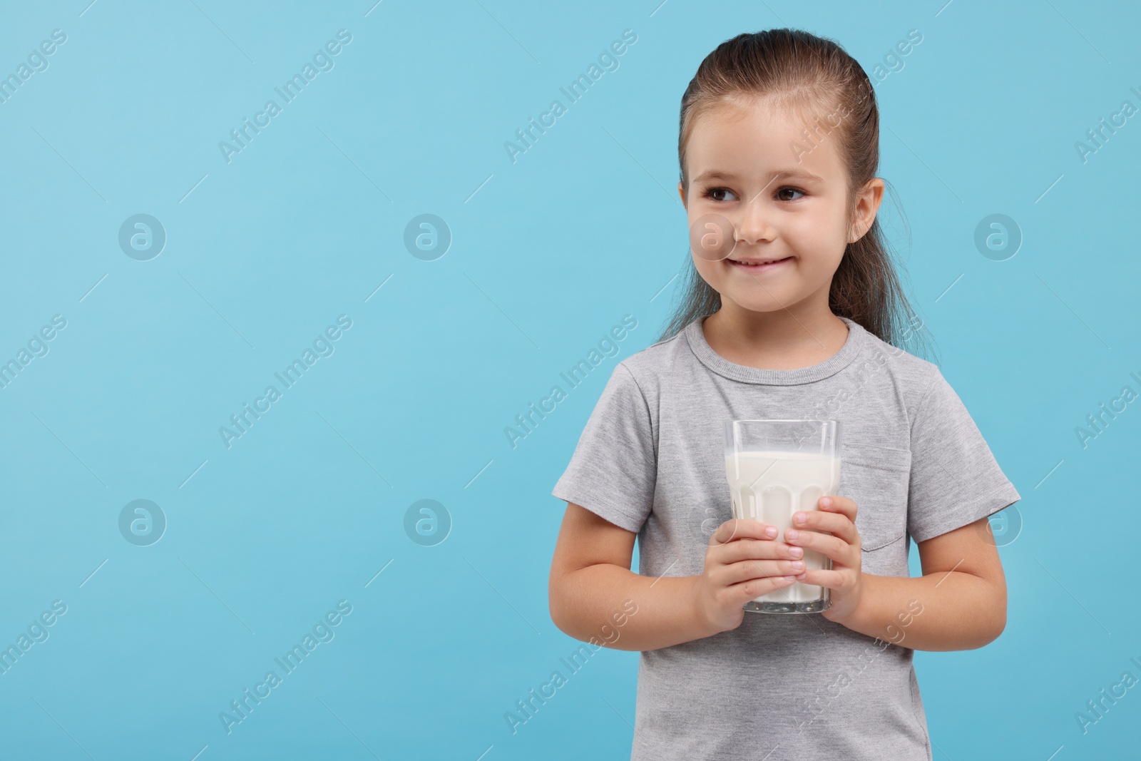 Photo of Cute girl with glass of fresh milk on light blue background, space for text