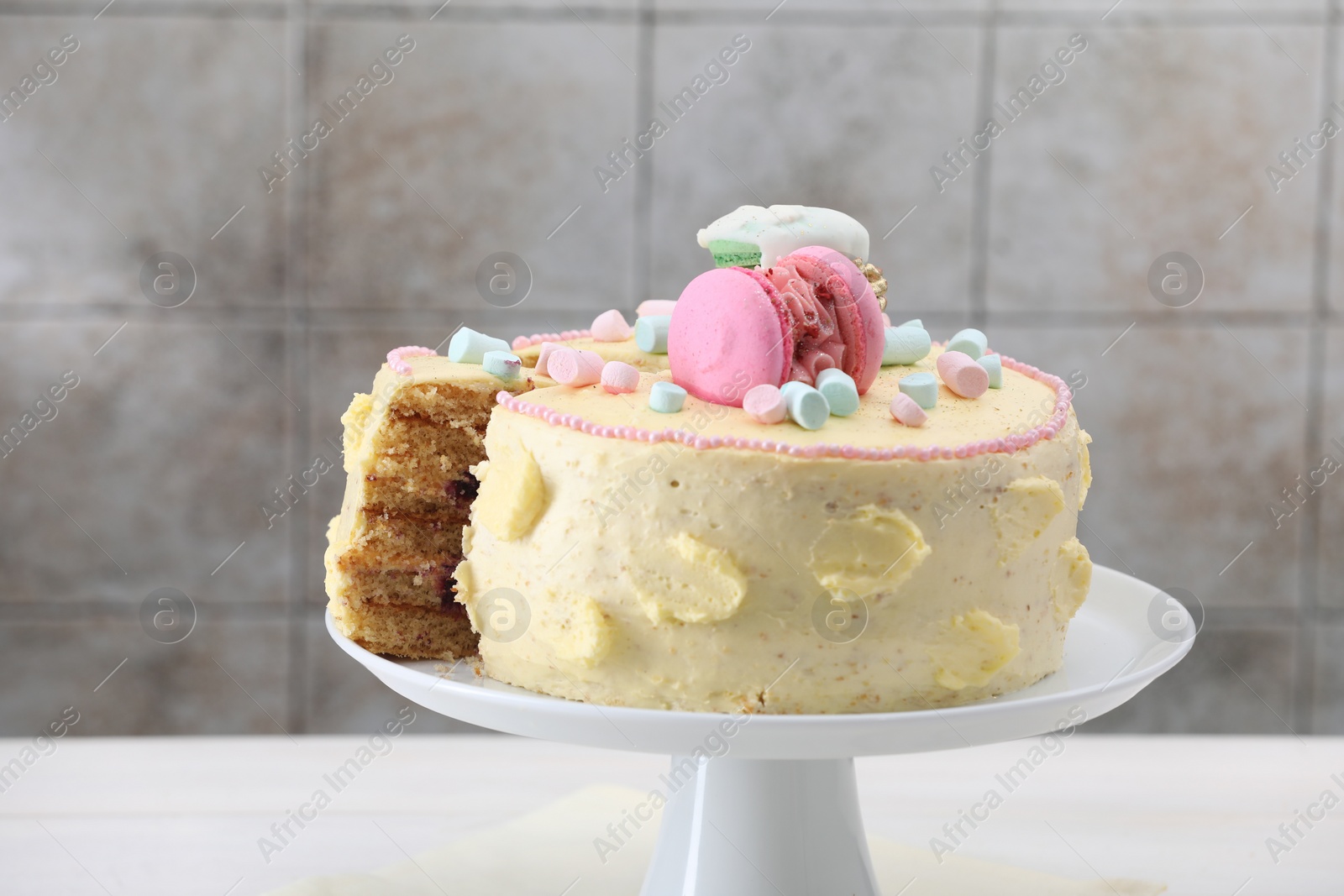 Photo of Delicious cake decorated with macarons and marshmallows on white table against tiled background, closeup