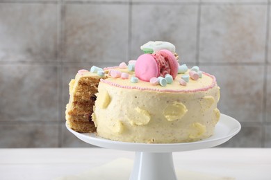 Delicious cake decorated with macarons and marshmallows on white table against tiled background, closeup