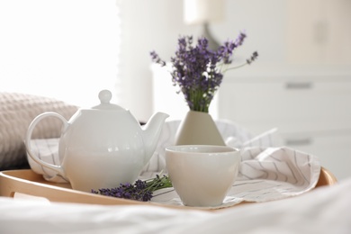 Wooden tray with cup of hot tea and beautiful lavender flowers on bed. Tasty breakfast