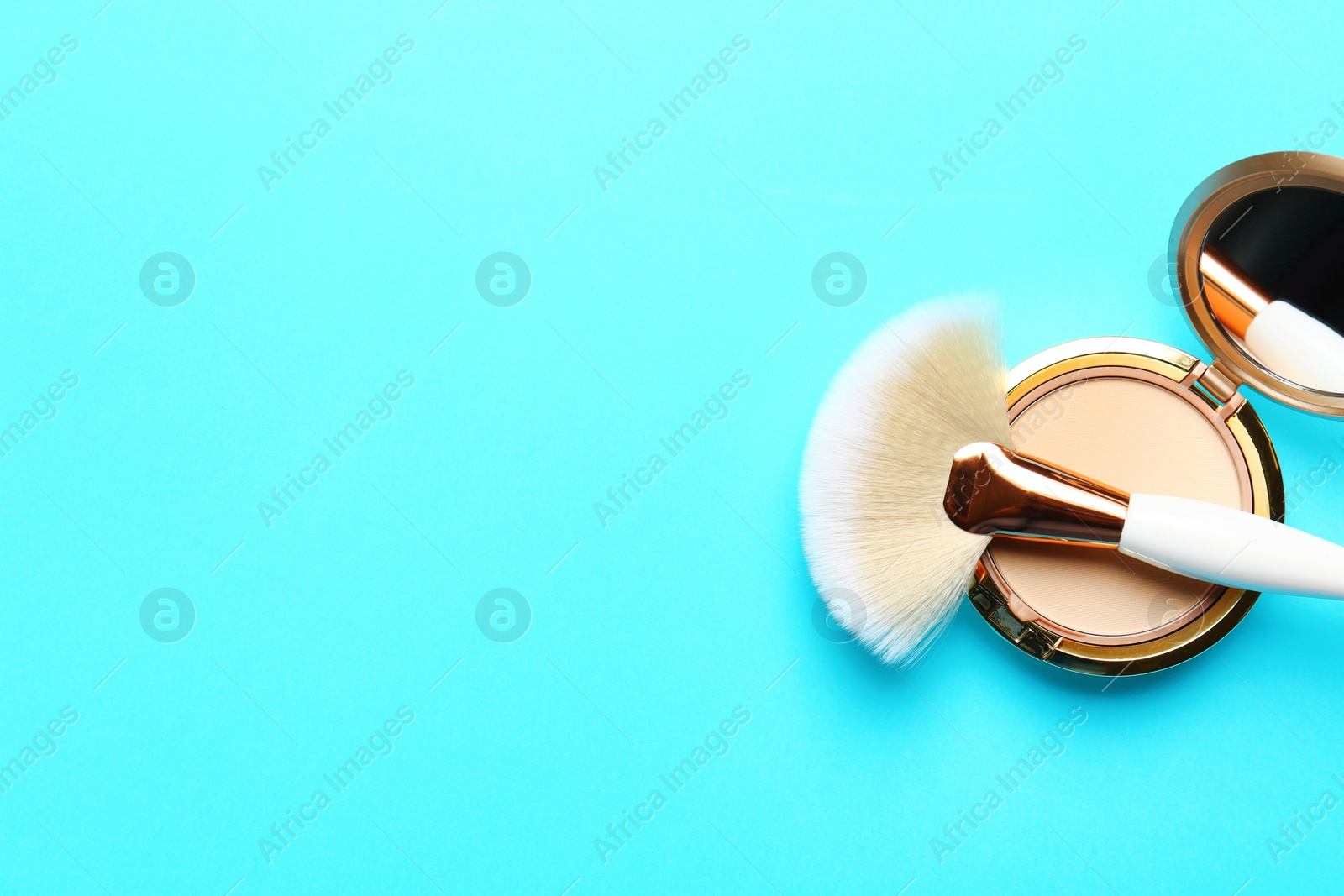 Photo of Professional makeup brush and face powder on light blue background, top view. Space for text