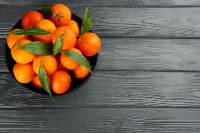 Fresh tangerines with green leaves on grey wooden table, top view. Space for text