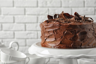 Stand with tasty homemade chocolate cake near white brick wall