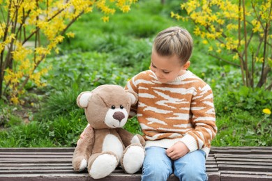 Photo of Little girl with teddy bear on wooden bench outdoors