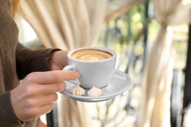 Photo of Young woman with cup of delicious coffee indoors