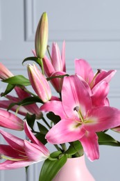Photo of Beautiful pink lily flowers in vase against light wall, closeup