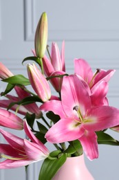 Beautiful pink lily flowers in vase against light wall, closeup