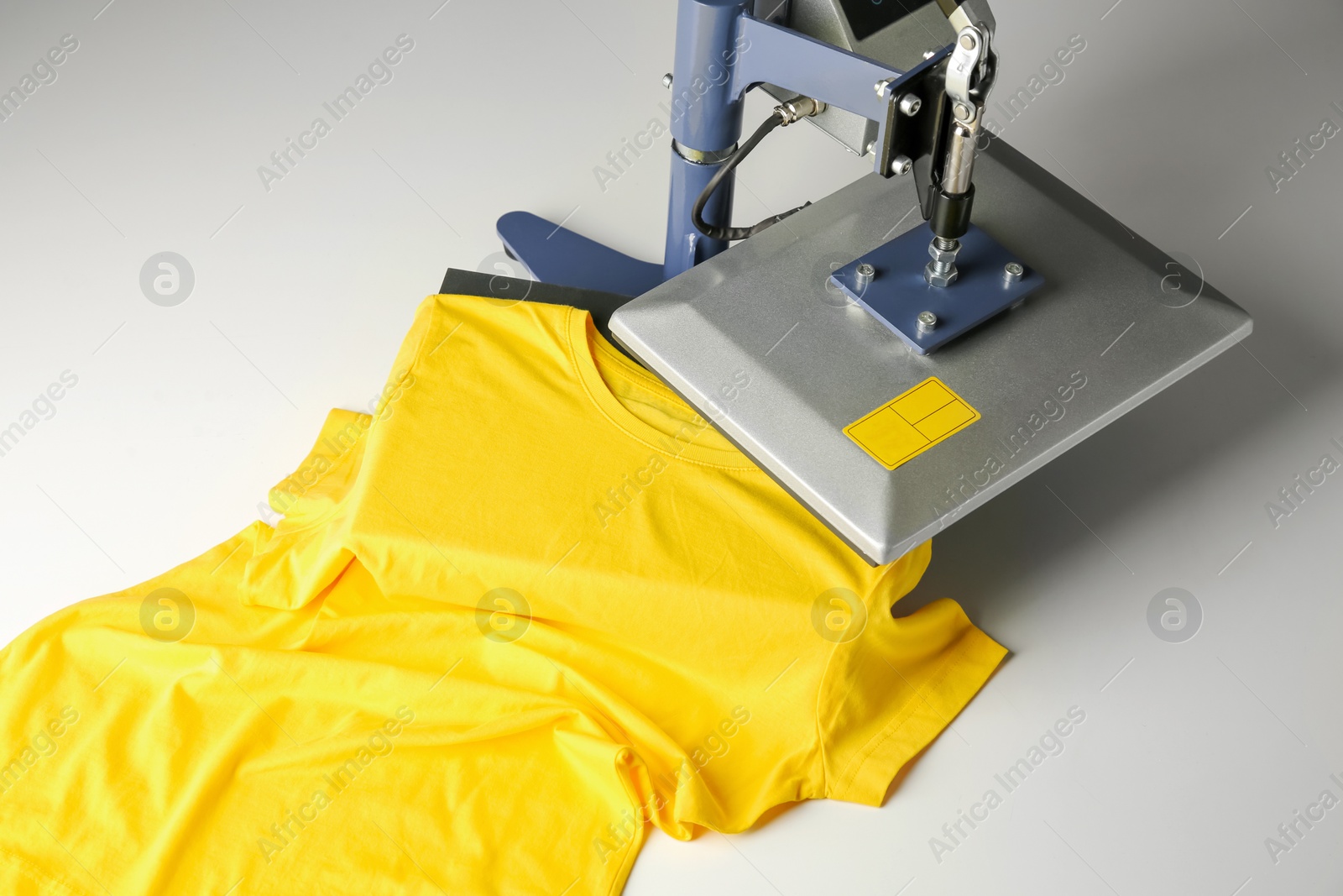 Photo of Printing logo. Heat press with yellow t-shirt on white table