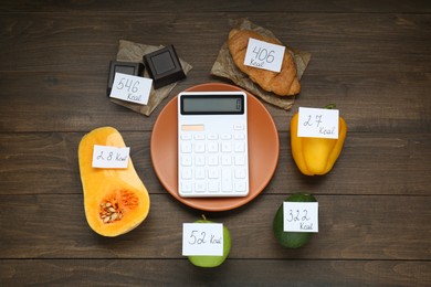 Photo of Calculator and food products with calorific value tags on wooden table, flat lay. Weight loss concept
