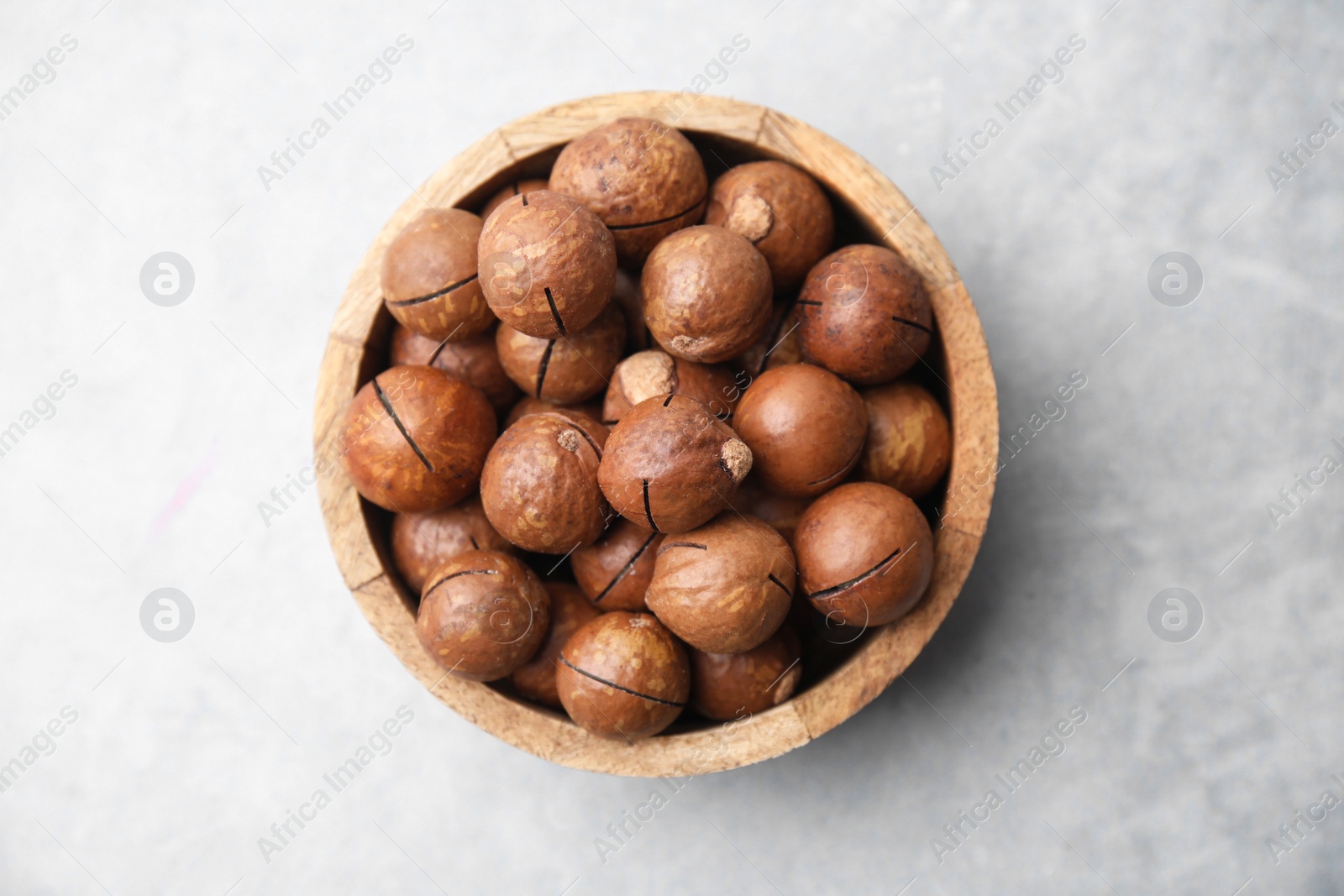 Photo of Delicious macadamia nuts in bowl on light grey table, top view