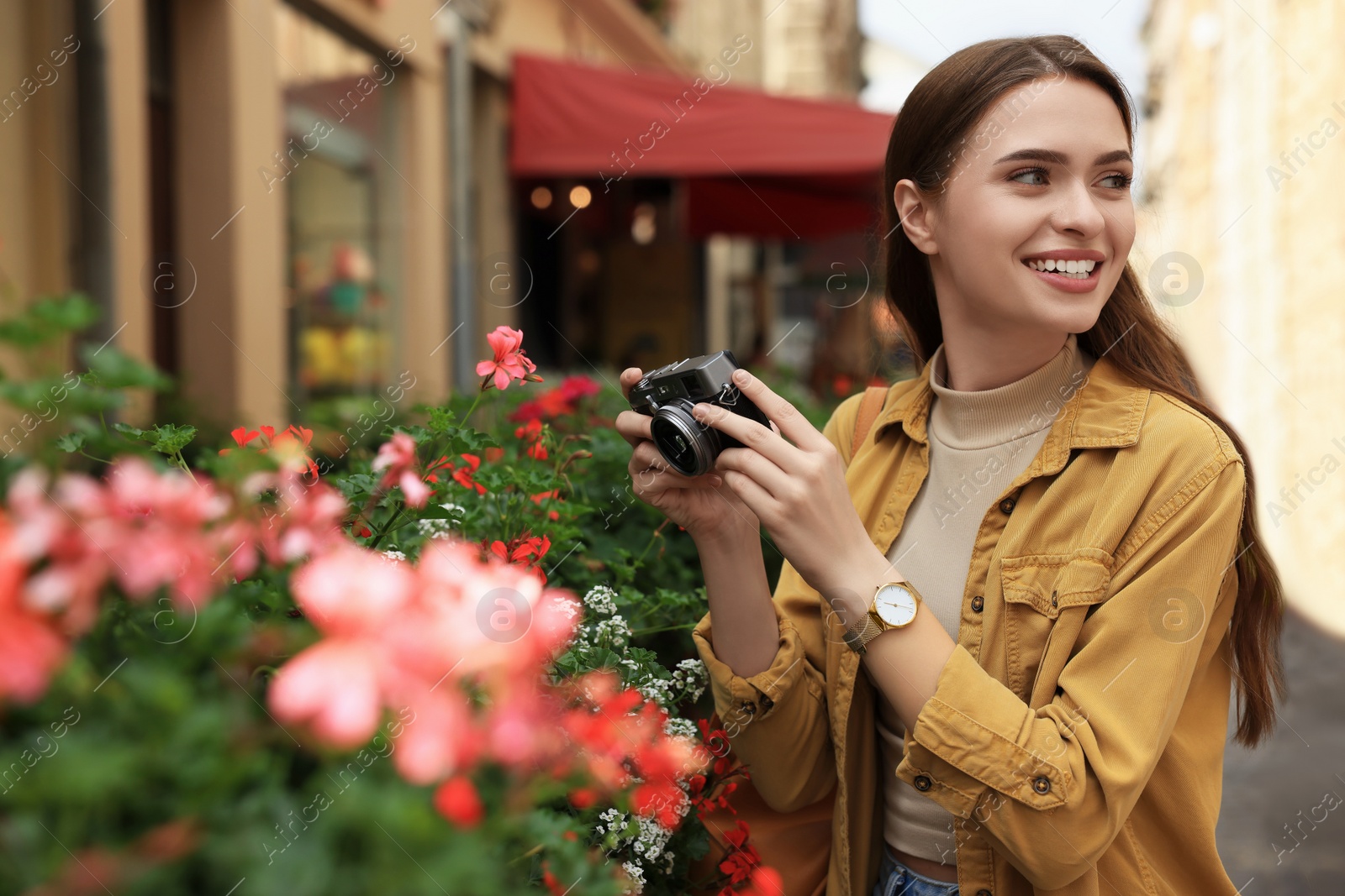 Photo of Young woman with camera taking photo of beautiful flowers on city street. Interesting hobby