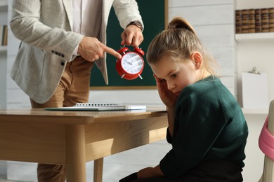 Teacher with alarm clock scolding pupil for being late in classroom