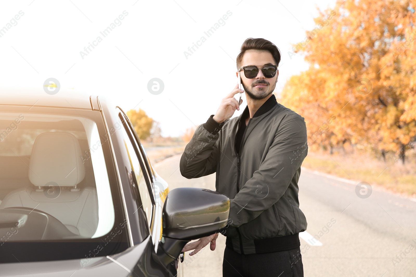 Photo of Young man talking on phone while opening car door, outdoors