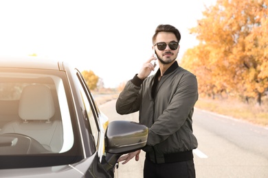 Photo of Young man talking on phone while opening car door, outdoors