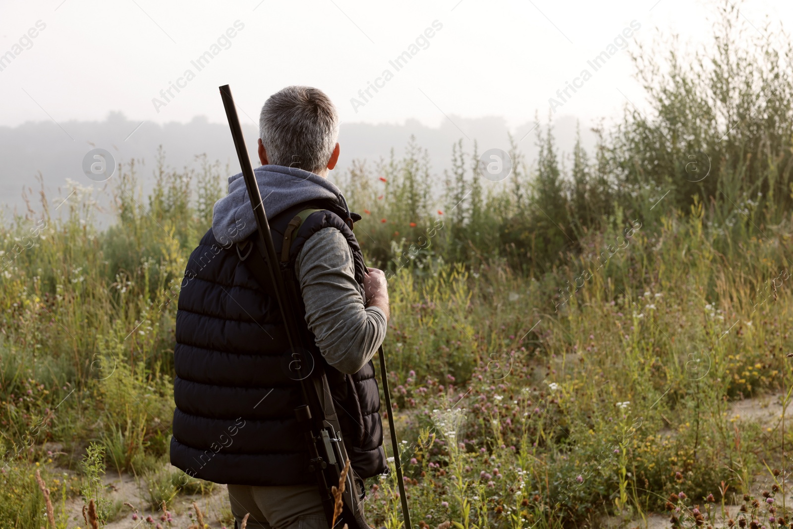 Photo of Man with hunting rifle outdoors, back view. Space for text