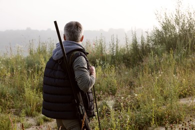 Photo of Man with hunting rifle outdoors, back view. Space for text