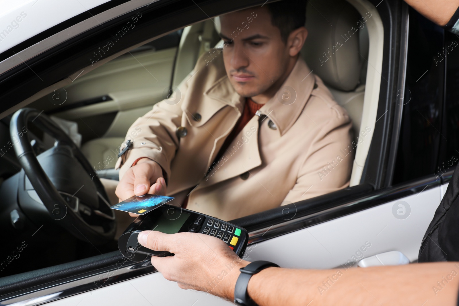 Photo of Man sitting in car and paying with credit card at gas station, focus on hands