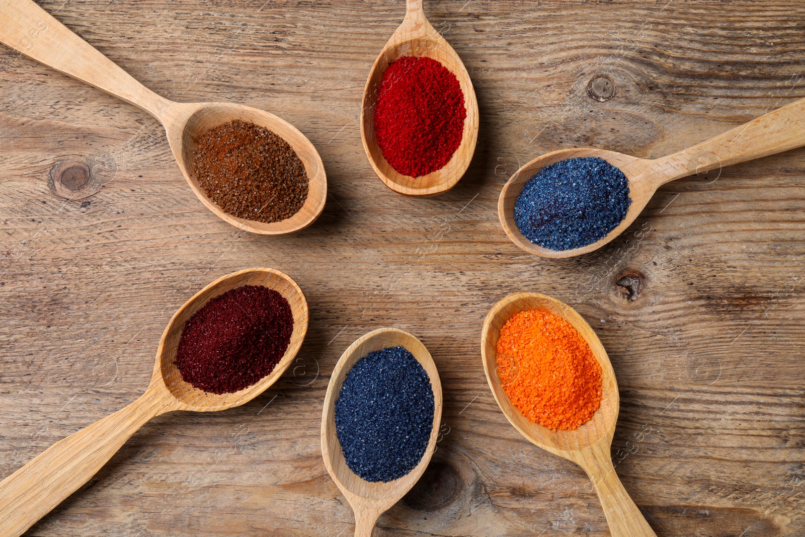 Photo of Many spoons with food coloring on wooden table, flat lay