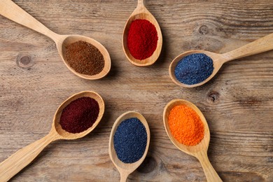 Many spoons with food coloring on wooden table, flat lay