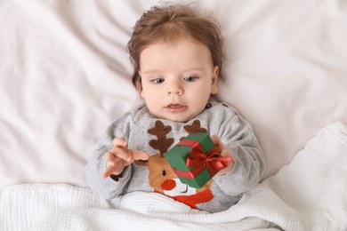 Photo of Cute little baby with gift on soft bed, top view