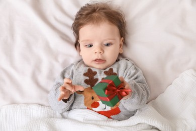 Cute little baby with gift on soft bed, top view