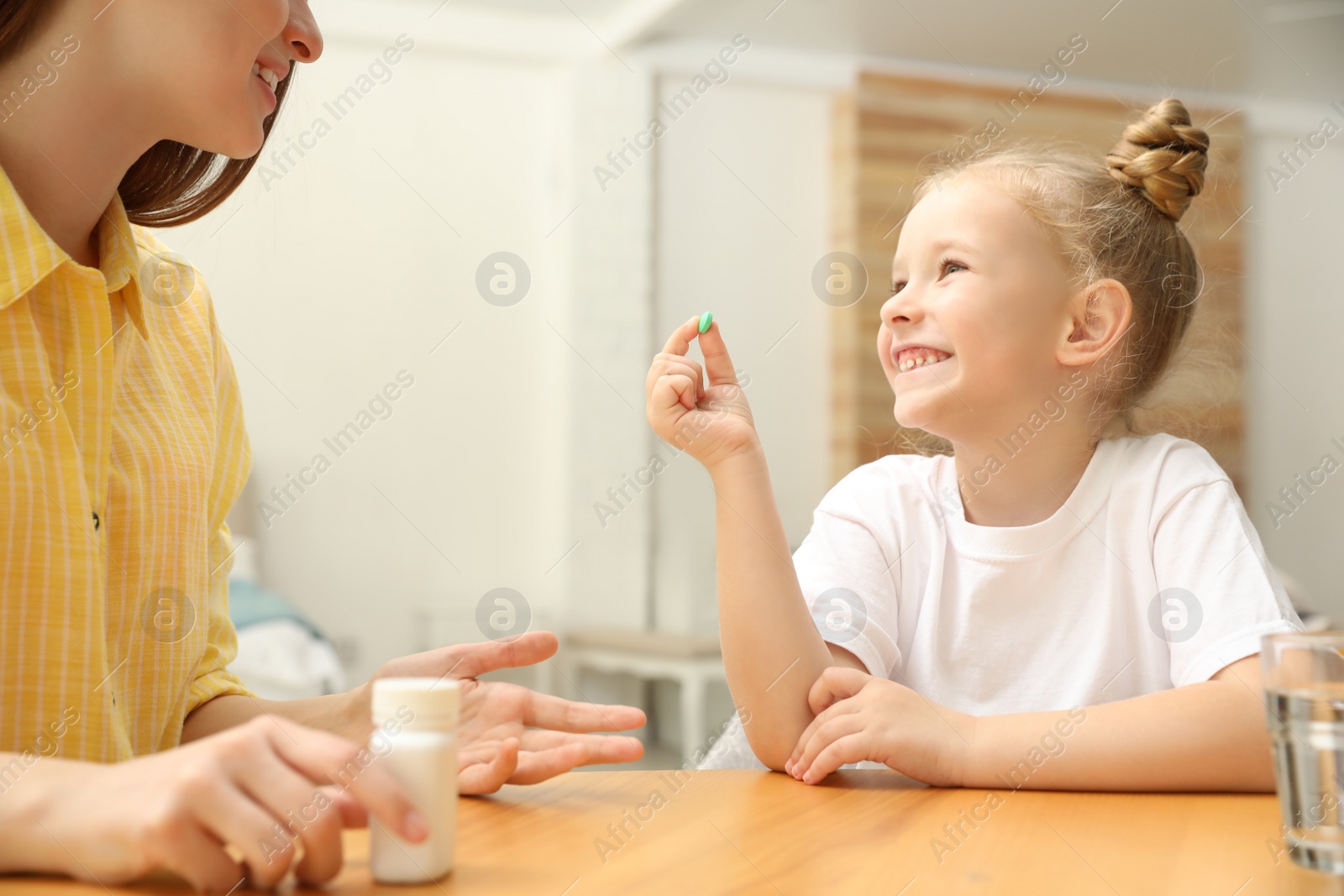 Photo of Young mother and her daughter with vitamin pill at home