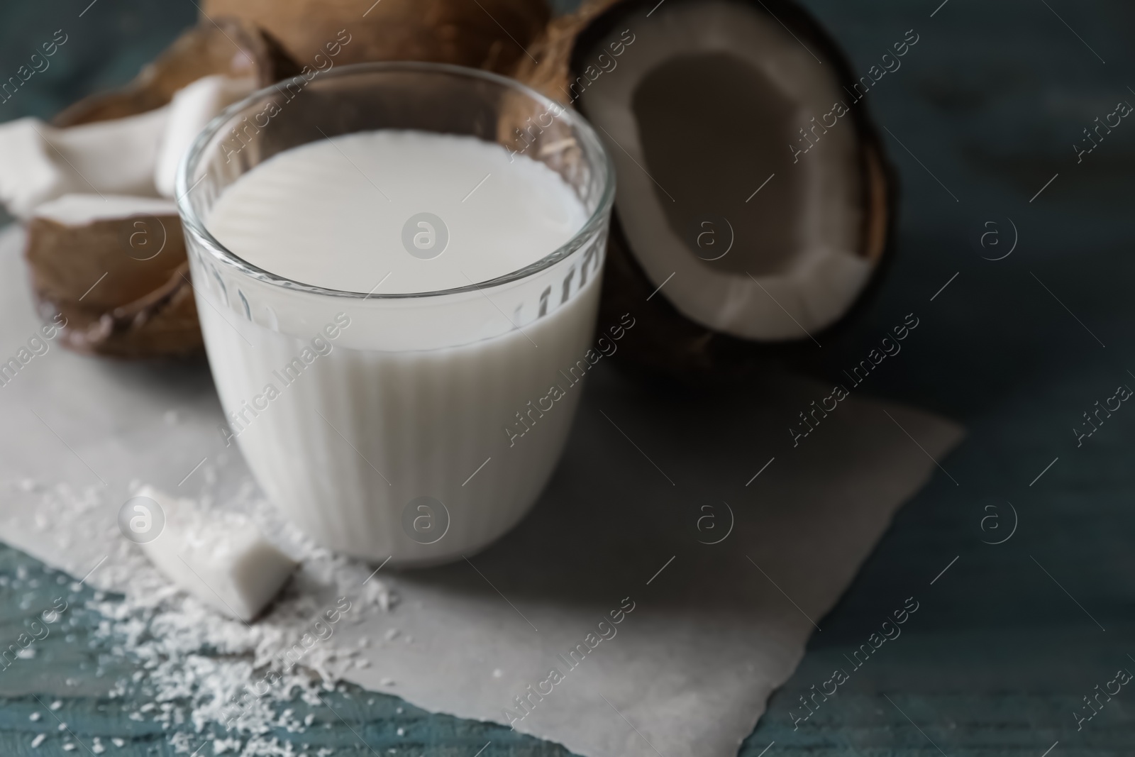 Photo of Glass of delicious coconut milk, flakes and nuts on wooden table, closeup. Space for text