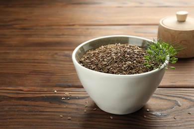 Photo of Bowl of dry seeds and fresh dill on wooden table, closeup. Space for text
