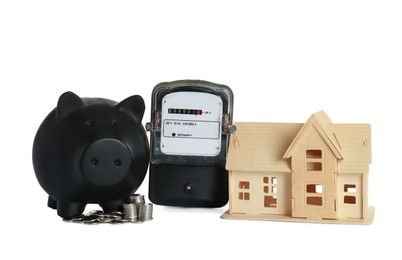 Electricity meter, house model, piggy bank and coins on white background
