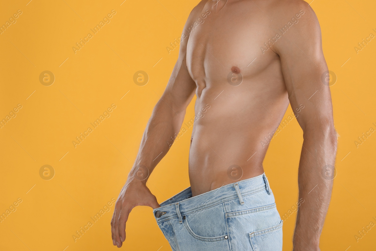 Photo of Shirtless man with slim body wearing big jeans on yellow background, closeup