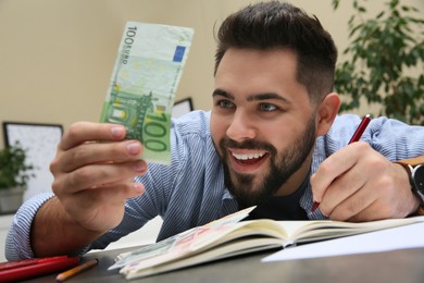 Photo of Young man with money at table indoors