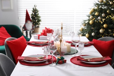 Photo of Christmas table setting with burning candles, gift box and dishware indoors