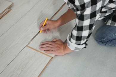 Professional worker using pencil during installation of new laminate flooring, closeup