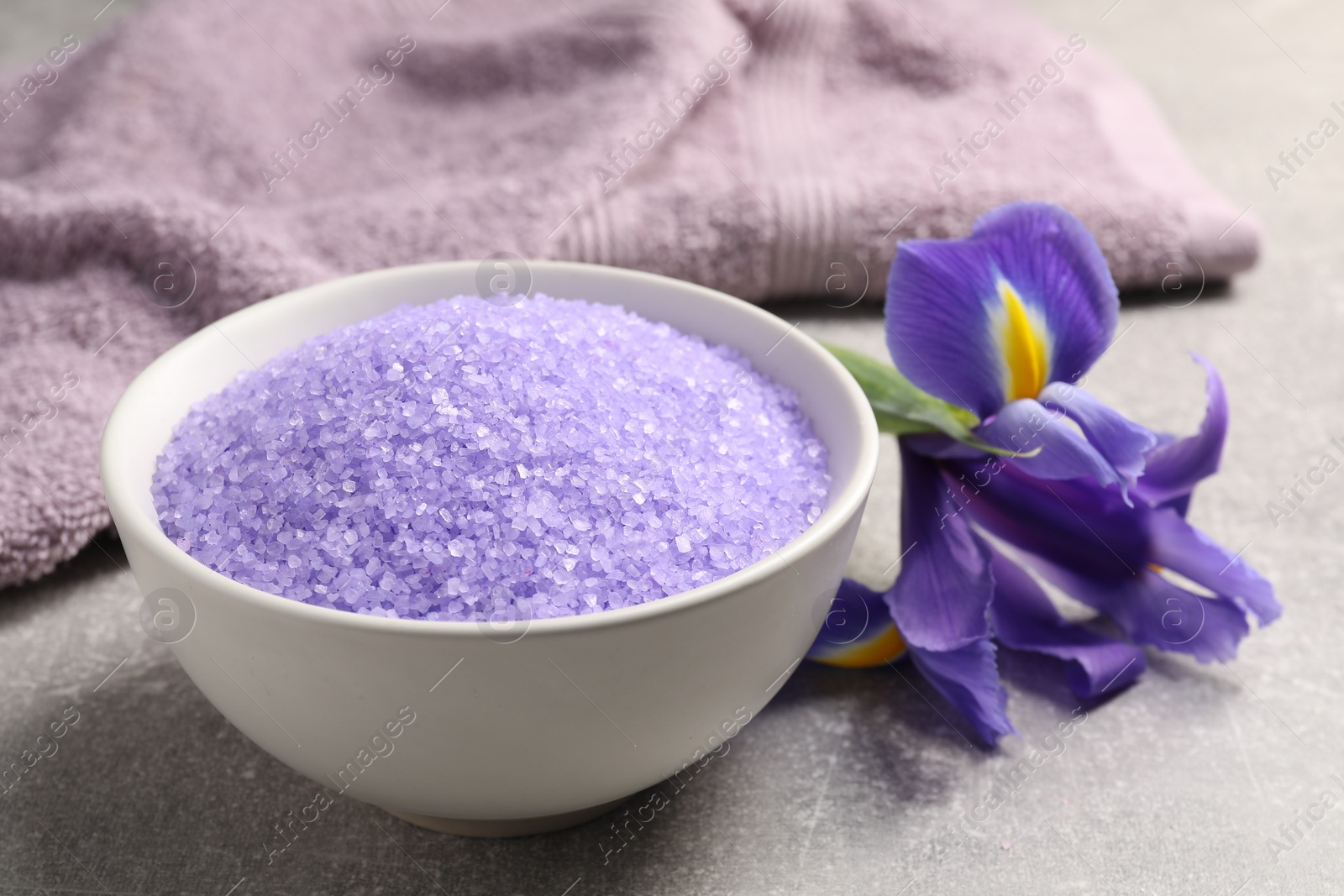 Photo of Natural sea salt in bowl, towel and beautiful flower on grey table, closeup