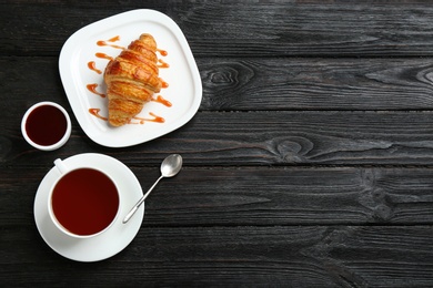 Photo of Plate with tasty croissant, cup of tea and space for text on dark wooden table, flat lay. French pastry