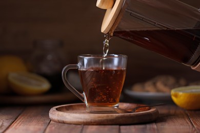 Pouring delicious tea into glass cup on wooden table, closeup