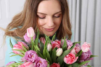 Happy young woman with bouquet of beautiful tulips indoors