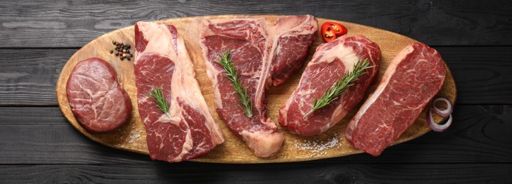 Photo of Pieces of raw beef meat and spices on black wooden table, top view