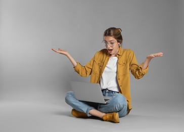 Photo of Emotional young woman with laptop on grey background
