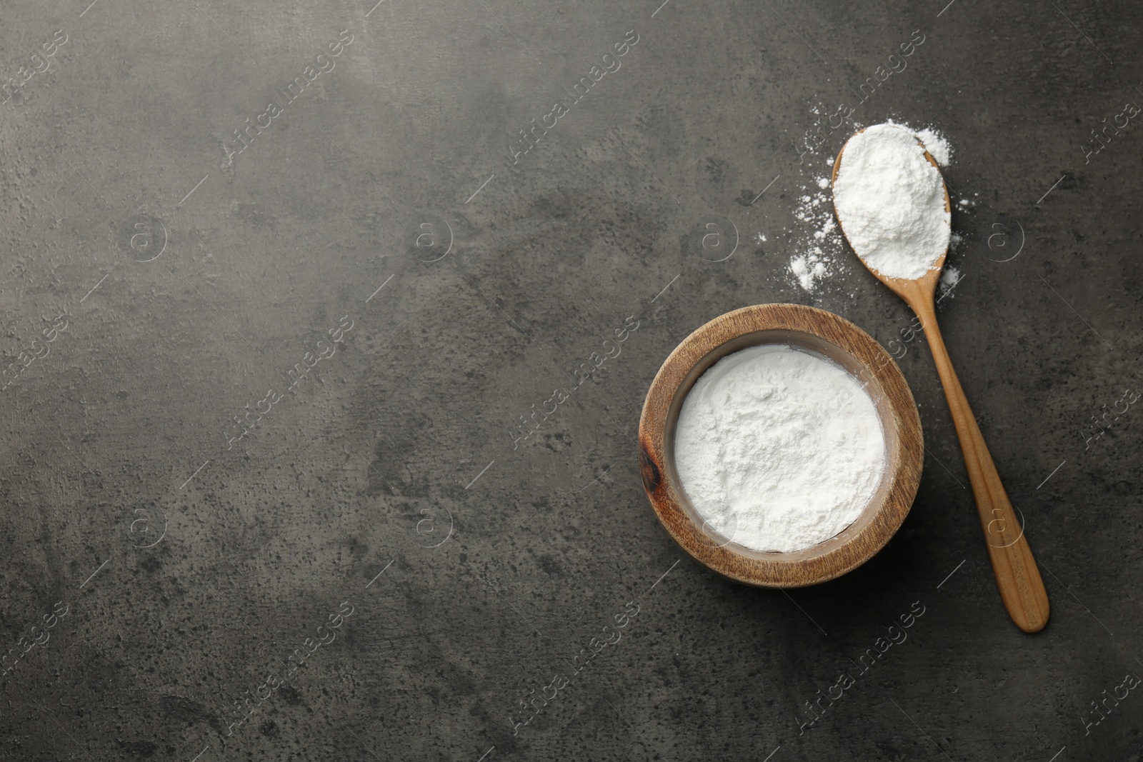 Photo of Baking powder in bowl and spoon on grey textured table, top view. Space for text