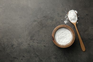 Baking powder in bowl and spoon on grey textured table, top view. Space for text