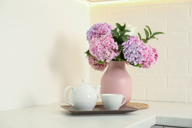 Beautiful bouquet of hydrangea flowers and tea on light countertop