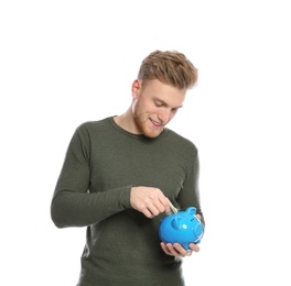 Young man putting money into piggy bank on white background