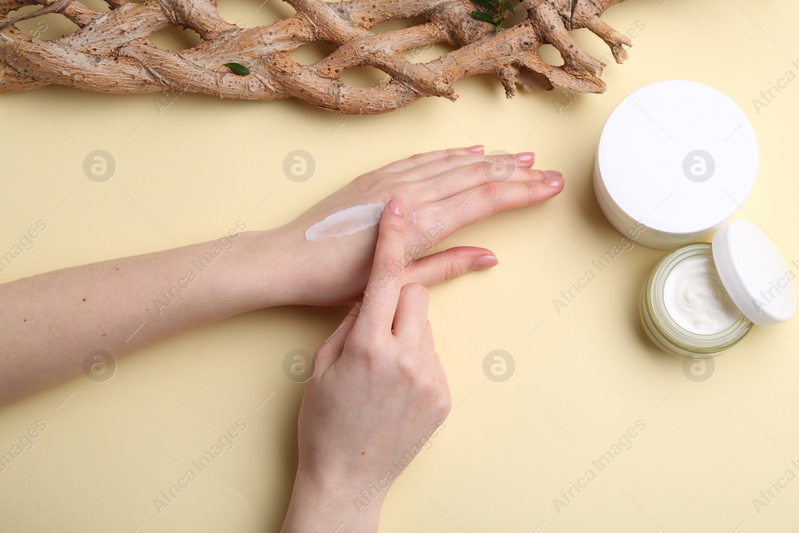 Photo of Woman applying hand cream on beige background, top view